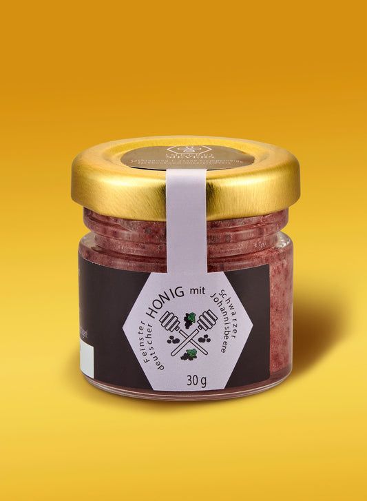 Ekovita Premium Honig mit Schwarzer Johannisbeere in einem Glas mit goldener Textur und frischen Beeren